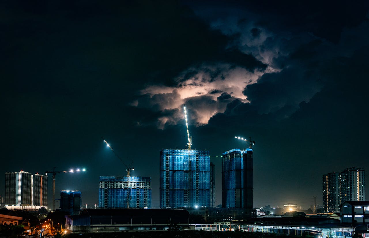Dramatic city skyline during a nighttime thunderstorm with construction in progress.
